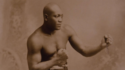 A sepia-toned photo of Jack Johnson posing in a boxing stance. | Video