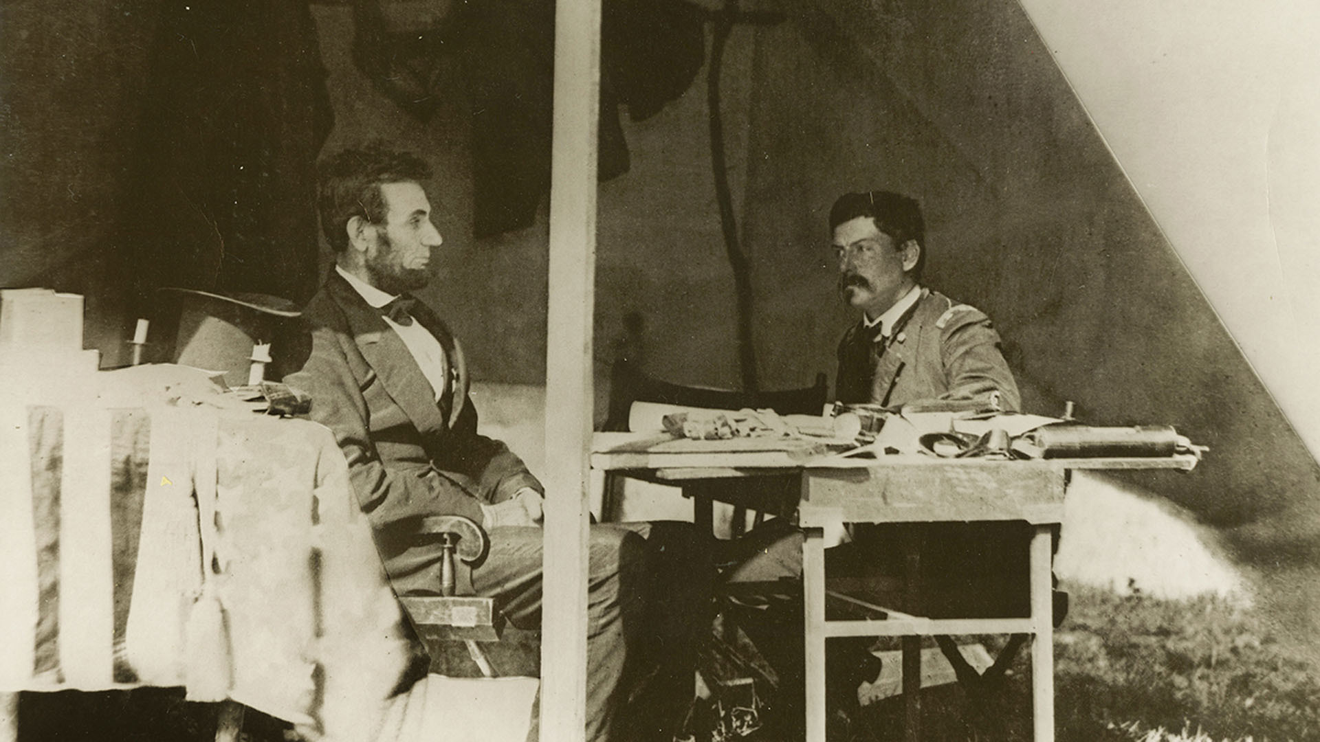 A sepia-toned photo showing Abraham Lincoln and General George McClellan seated, looking at one another, in Antietam, Maryland, circa 1862.