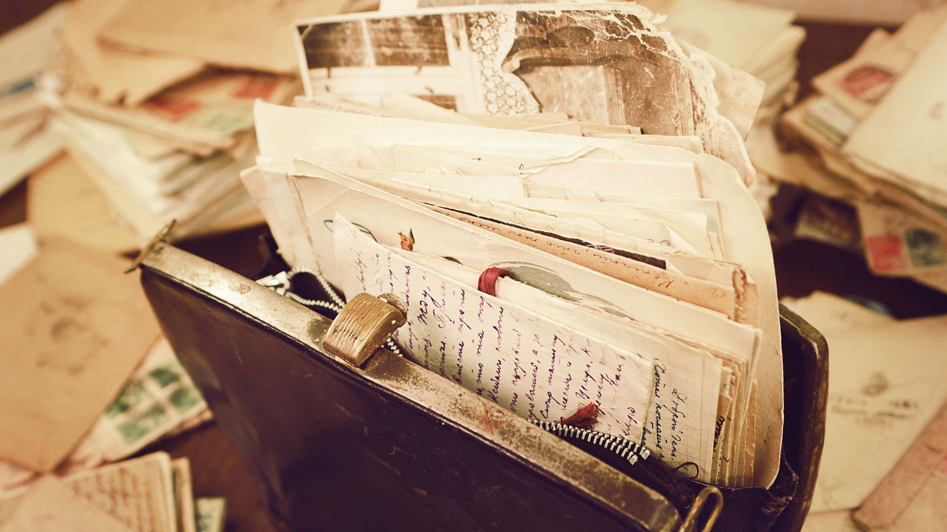 A color photo of old, time-worn letters stuffed into a brown leather case. Surrounding it are other old letters strewn about on the table.