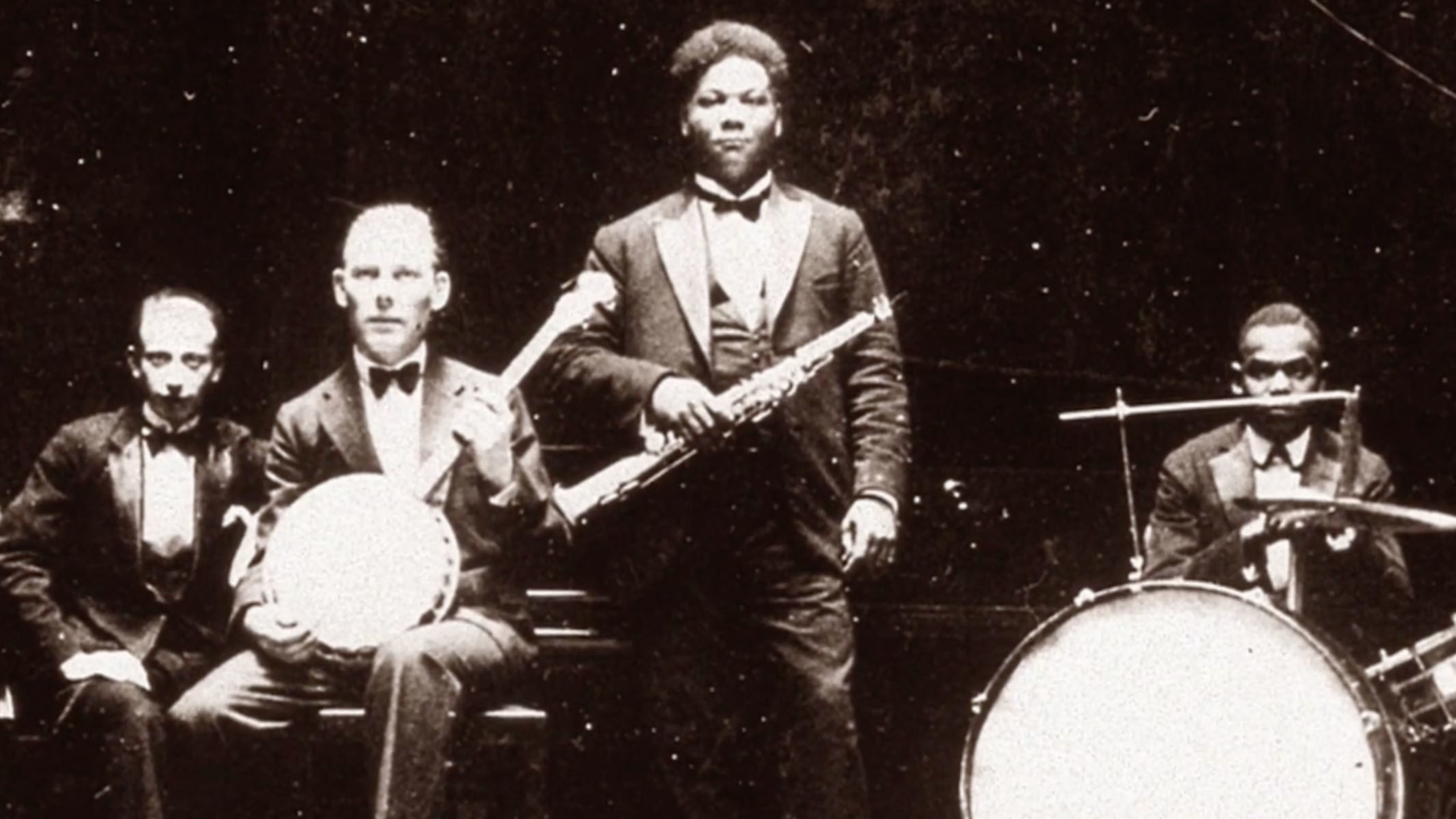 A black-and-white image of 4 men posing for a photograph, holding musical instruments.