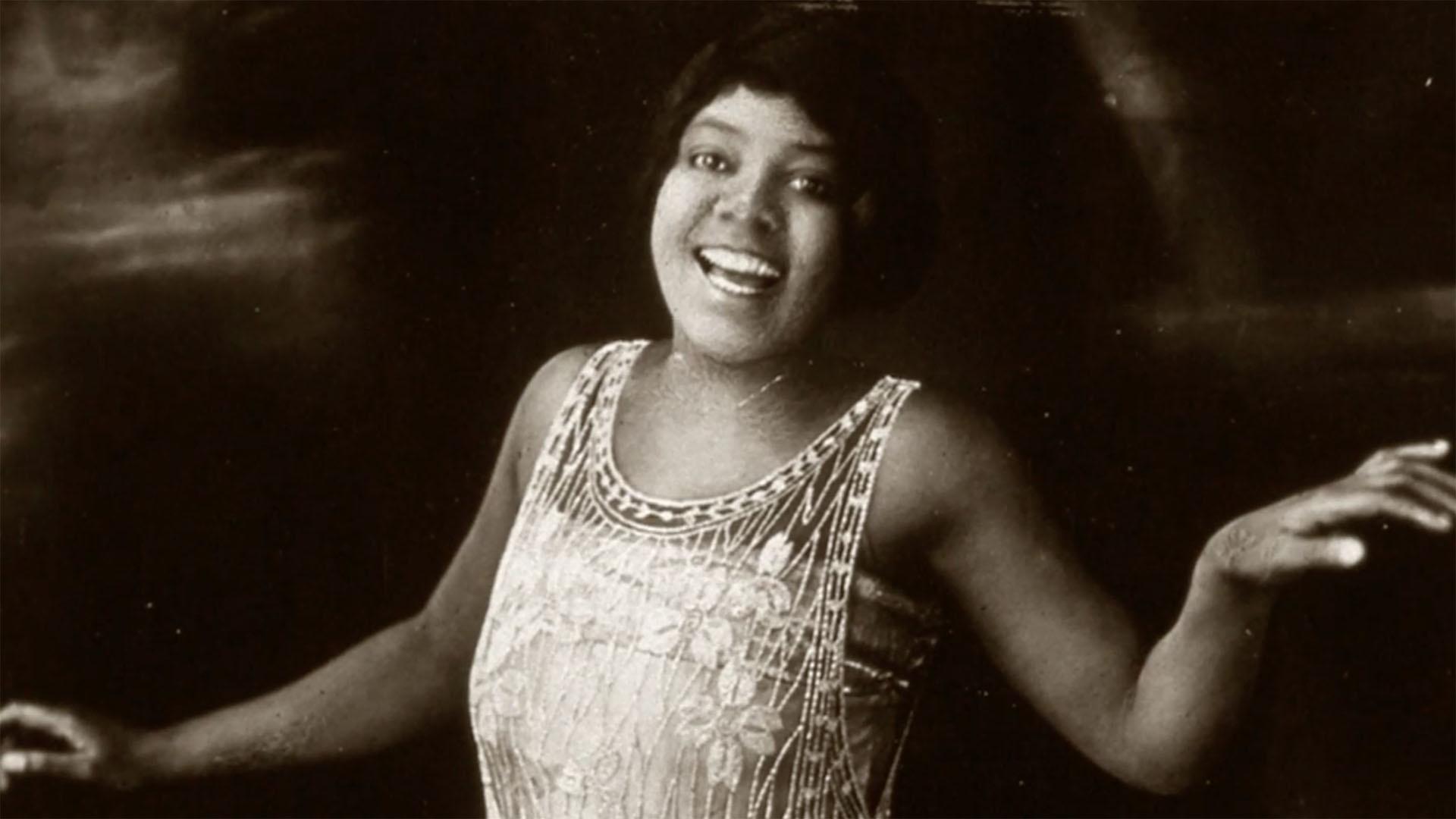 A black-and-white photo of a young woman in a 1920s style flapper dress, smiling and dancing.