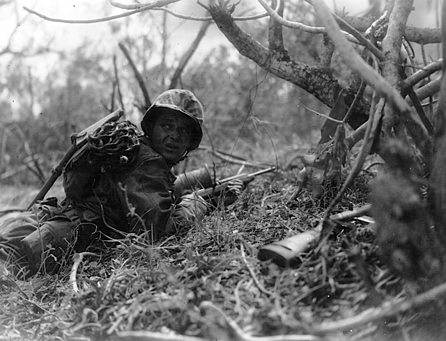 A cautious Marine, armed with a scaling rope, advances toward Mount Tapochau on Saipan. June 1944.