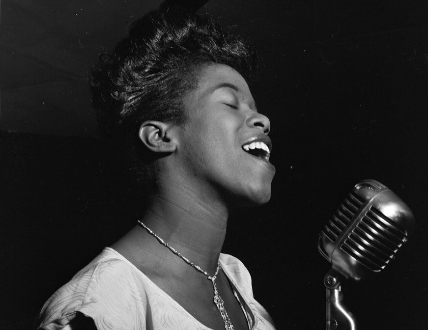 A black and white photo of Sarah Vaughan singing into a microphone, possibly at Cafe Society, NYC, ca. August 1946.