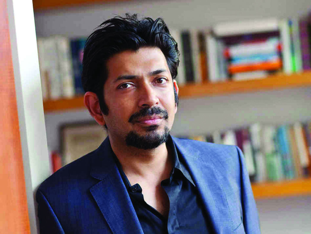 Photograph of Dr. Siddhartha Mukherjee with a bookshelf in the background.