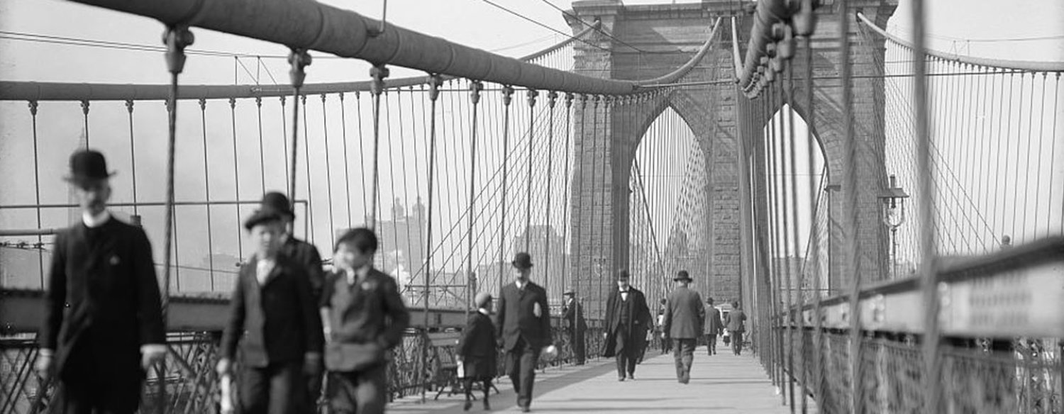 A black-and-white photo of people crossing the Brooklyn Bridge in the early 20th century.