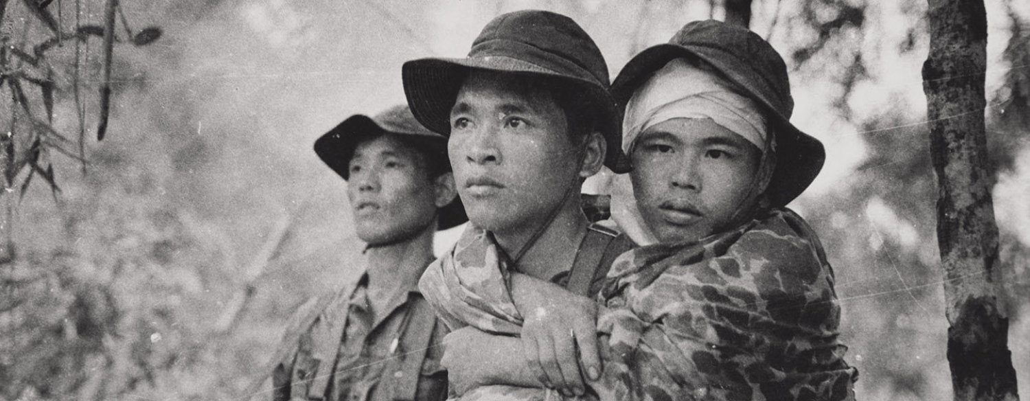 A black-and-white photo of three Vietnamese men standing amidst thick foliage. Their expressions are serious.