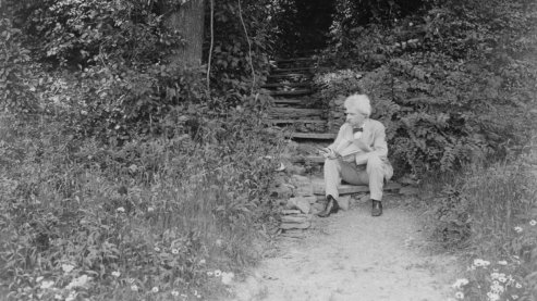 A black-and-white photo of Mark Twain sitting on outdoor steps along a secluded garden path, surrounded by greenery. He is looking away from the camera. | Timeline