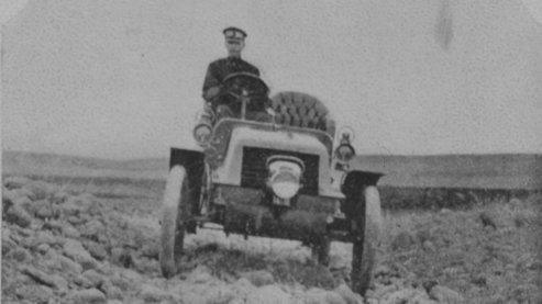 A black-and-white photo of Horatio Nelson Jackson driving an old-fashioned car toward the camera. | The Car