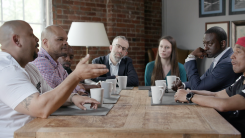 Seven people sitting around a table; the first man on the left is speaking and gesturing with his right hand | The Central Park Five on UNUM