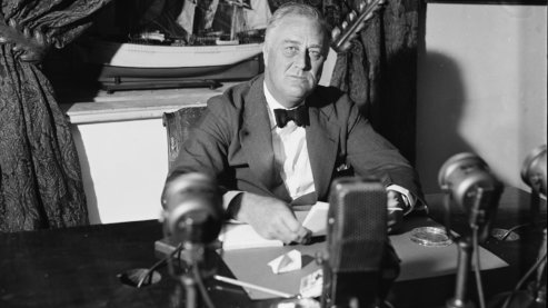 A black-and-white photo showing President Franklin Delano Roosevelt sitting behind a bank of radio microphones in the White House on September 6, 1936. | FDR's Fireside Chats